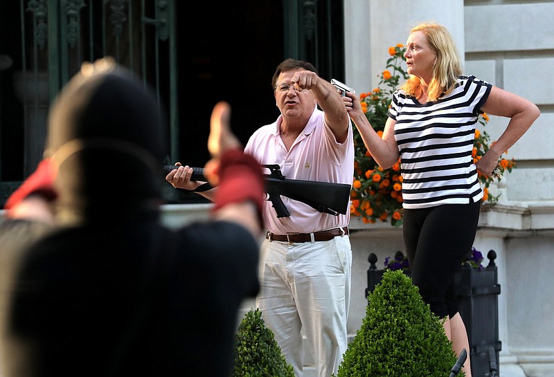 FILE - In this June 28, 2020 file photo, armed homeowners Mark and Patricia McCloskey, standing in front their house along Portland Place confront protesters marching to St. Louis Mayor Lyda Krewson's house in the Central West End of St. Louis. Missouri Chief Disciplinary Counsel Alan Pratzel is asking the state Supreme Court to suspend the law licenses of Mark and Patricia McCloskey, the St. Louis couple who gained national attention last year when they waved guns at racial injustice protesters outside their home. (Laurie Skrivan/St. Louis Post-Dispatch via AP)