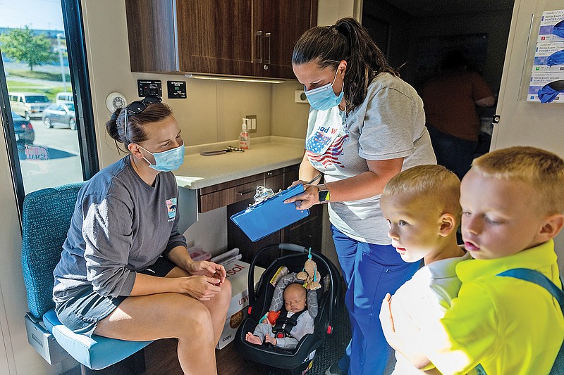 <p>Ethan Weston/News Tribune</p><p>Medical assistant Lacey Flaugher explains a form Wednesday to Ashley Forck as her kids wait for their mother to get her first COVID-19 vaccine at the Boys & Girls Club of Jefferson City vaccination clinic.</p>