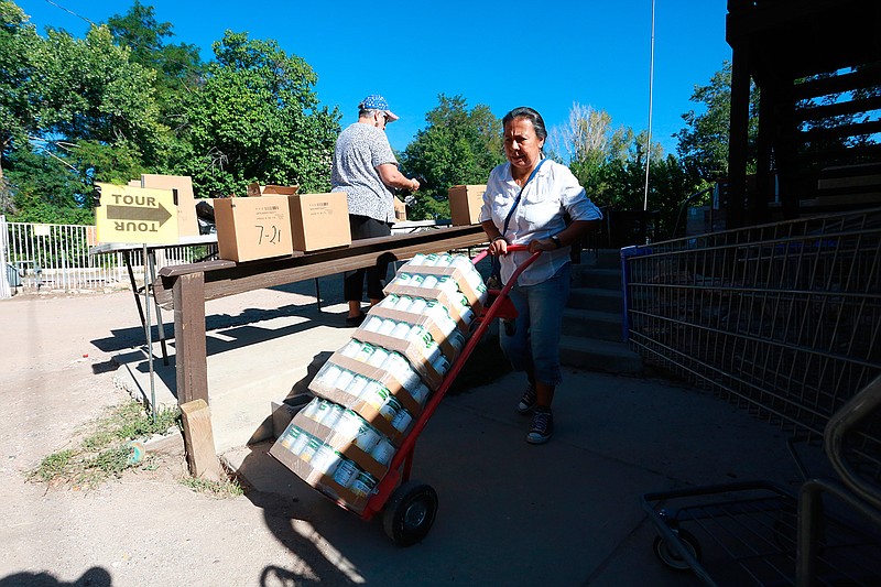 Barrios Unidos president Lupe Salazar pushes a dolly filled with canned food ahead of a food drive on Thursday, Sept. 23, 2021, in Chimay, New Mexico. (AP Photo/Cedar Attanasio)