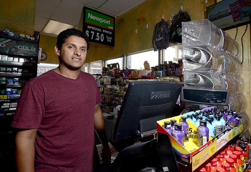 Store clerk Jacob Aziz, who sold an $80,000 winning lottery ticket, poses for a photo behind the register at the Express Way 2 at the corner of Delaware Avenue and Anna Drive in McComb, Miss., on Tuesday, Sept. 21, 2021. (Matt Williamson//The Enterprise-Journal via AP)