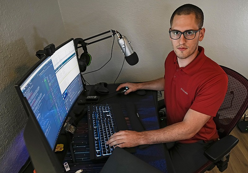 In this Sept. 20, 2021, photo Austin Moody poses for a photo as he sits a his home work station in Tampa, Fla. Moody, the Michigan native, got a scholarship from the Department of Defense that required working for the agency at least a year after graduating. Moody said he understands that state governments don't have the kind of money that federal agencies or private companies spend on recruiting and generous salaries. (AP Photo/Steve Nesius)