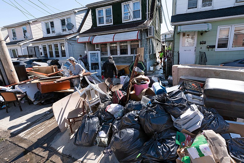 In this Sept. 3, 2021 file photo, people clear debris and damaged belongings from their homes in the Queens borough of New York. Floodwaters from the remnants of Hurricane Ida have long receded but Northeast residents still in the throes of recovery are being hit with another unexpected blow: Thousands of families without flood insurance are now swamped with financial losses after runoff from the fierce storm submerged basements, cracked foundations and destroyed valuable belongings.  (AP Photo/Mark Lennihan, File)