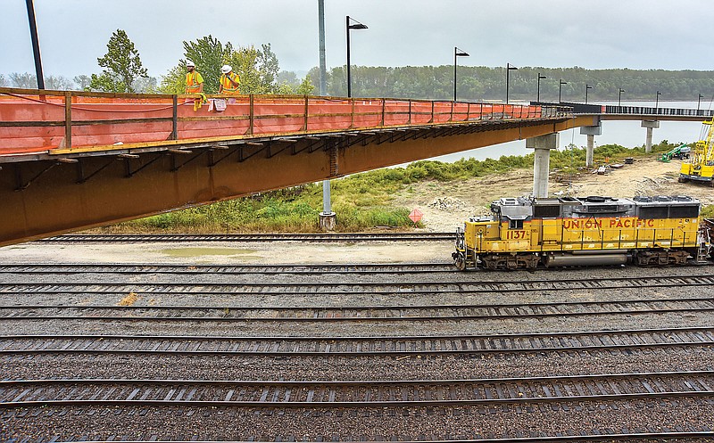 <p>Julie Smith/News Tribune</p><p>Construction workers Glenn Mundy, near, and Caleb Wells cross the nearly completed Bicentennial Bridge to Adrian’s Island on Monday. There is a delay in the projected opening date of the bridge due to a delay in manufacturing the mesh barrier that will serve as a safety enclosure to prevent anything from the bridge above being thrown at or onto trains passing under it.</p>