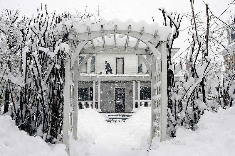 FILE - Amber Cox shovels snow from the porch roof at her home in Auburn, Maine, on March 8, 2018.  With prices surging worldwide for heating oil, natural gas and other fuels, the U.S. government said Wednesday, Oct. 13, 2021 it expects households to see jumps of up to 54% for their heating bills compared to last winter.  (Daryn Slover/Sun Journal via AP)