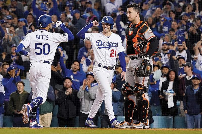 Mookie Betts is greeted by Dodgers teammate Walker Buehler as Giants catcher Buster Posey waits after Betts hit a two-run home run that scored Buehler during the fourth inning of Tuesday night's Game 4 of the National League Division Series in Los Angeles.