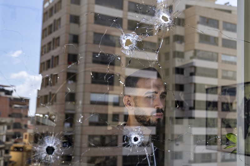 An employee looks through an office window riddled with bullet holes after the deadly clashes that erupted last Thursday along a former 1975-90 civil war front-line between Muslim Shiite and Christian areas, in Ain el-Rumaneh neighborhood, Beirut, Lebanon, Tuesday, Oct. 19, 2021. The shootout on the streets of Beirut between rival Christian and Muslim groups has revived memories of the country's 1975-90 civil war and fired up sectarian passions in a country that never dealt with the causes of its violent past. (AP Photo/Hassan Ammar)