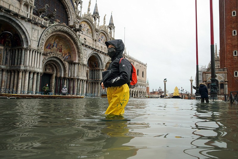 FILE - In this Tuesday, Dec. 8, 2020 file photo, people wade their way through water in flooded St. Mark's Square following a high tide, in Venice, Italy.  Lashing winds that pushed 1.87 meters (nearly 6 feet 2 inches) of water into Venice in November 2019 and ripped the lead tiles off St. Mark’s Basilica for the first time ever shocked Venetians with the city’s second-worst flood in history, but it was the additional four exceptional floods over the next six weeks that triggered fears about the impact of worsening climate change.  (Anteo Marinoni/LaPresse via AP, file)