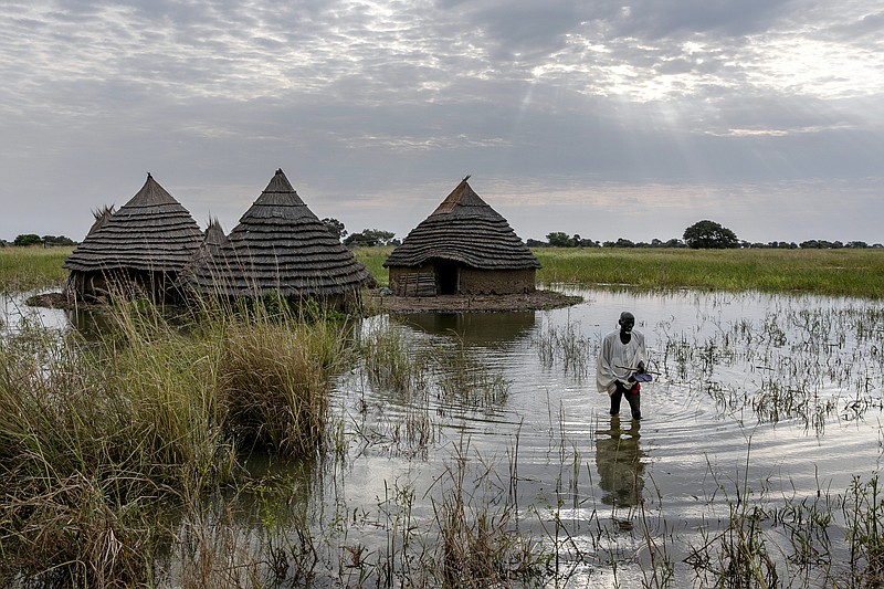 Yel Aguer Deng, who does not know his age, walks through water from his compound to the Wanyhok-Akon road, near Malualkon in Northern Bahr el Ghazal State, South Sudan, Wednesday, Oct. 20, 2021. The worst flooding that parts of South Sudan have seen in 60 years now surrounds his home of mud and grass. His field of sorghum, which fed his family, is under water. Surrounding mud dykes have collapsed. The United Nations says the flooding has affected almost a half-million people across South Sudan since May. (AP Photo/Adrienne Surprenant)