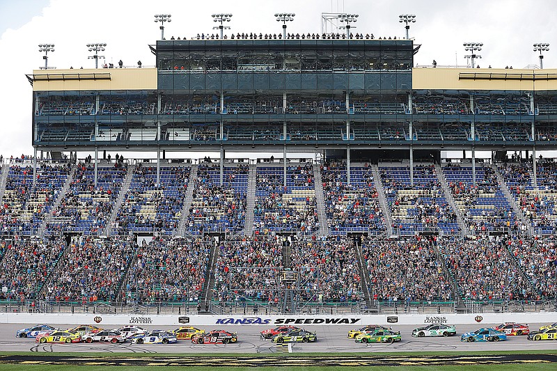 Fans watch from the grandstand as race cars cross the start/finish line at the start of Sunday afternoon's NASCAR Cup Series race at Kansas Speedway in Kansas City, Kan.