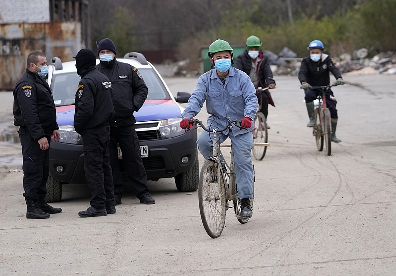 Vietnamese workers who are helping construct the first Chinese car tire factory in Europe ride bicycles past security officers near the northern Serbian town of Zrenjanin, 50 kilometers north of Belgrade, Serbia, Thursday, Nov. 18, 2021. Reports have emerged in Serbia of prison-like conditions for some 500 of them at the construction site in north of the country where China's Shandong Linglong Tire Co is building the huge factory. Populist-run Serbia is a key spot for China's expansion and investment policies in Europe and Chinese companies have kept a tight lid on their projects in the country amid reports of disrespect of the Balkan nation's anti-pollution laws and labor regulations. (AP Photo/Darko Vojinovic)