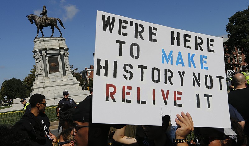 FILE - In this Saturday, Sept. 16, 2017 file photo, protesters hold signs in front of the statue of Confederate General Robert E. Lee on Monument Avenue in Richmond, Va.  A jury began deliberations Friday, Nov. 19, 2021 in a civil trial of white nationalists accused of conspiring to commit racially motivated violence at the deadly “Unite the Right" rally in Charlottesville four years ago.(AP Photo/Steve Helber, File)