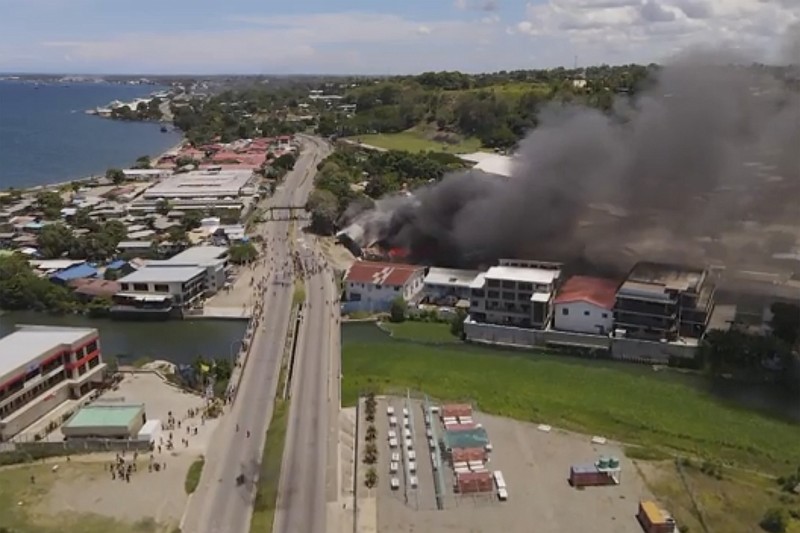 In this image made from aerial video, smoke rises from burning buildings during a protest in the capital of Honiara, Solomon Islands, Thursday, Nov. 25, 2021. Prime Minister Manasseh Sogavare declared a lockdown after about 1,000 people took to the streets in the capital for a second day, demanding his resignation over a host of domestic issues, according to local media reports. (Australian Broadcasting Corporation via AP)