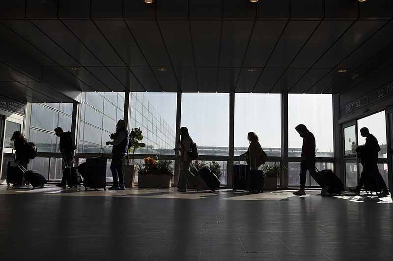 Travelers walk with their luggage in the Ben Gurion Airport near Tel Aviv, Israel, Sunday, Nov. 28, 2021. Israel on Sunday approved barring entry to foreign nationals and the use of controversial technology for contact tracing as part of its efforts to clamp down on a new coronavirus variant. (AP Photo/Ariel Schalit)