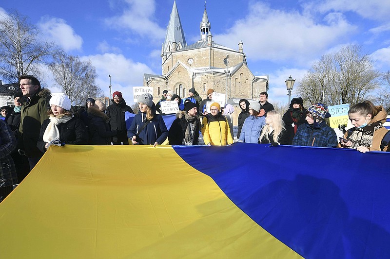 People hold a huge Ukrainian national flag during a protest in support of Ukraine in front of the Russian General Consulate in Narva, Estonia, Saturday, Feb. 26, 2022. Russian troops stormed toward Ukraine's capital Saturday, and street fighting broke out as city officials urged residents to take shelter. (AP Photo/Sergei Stepanov)