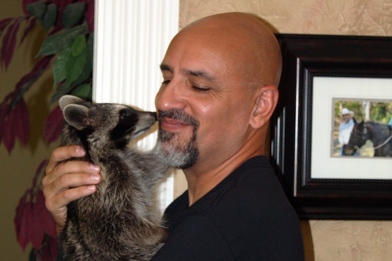 Billy Smith smiles as pet raccoon Peggy touches his face Thursday, Sept. 8 2022, at Smith's home in Fouke, Ark. The young raccoon is a contest in the America's Favorite Pet contest. (Staff photo by Mallory Wyatt)