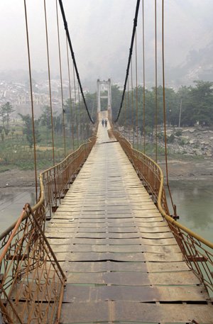 Two people walk Saturday on an earthquake-damaged bridge in China's Sichuan province.