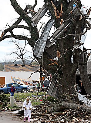 Kathy Phillips rushes Friday past a tree filled with wreckage from Thursday's tornado in Mena.