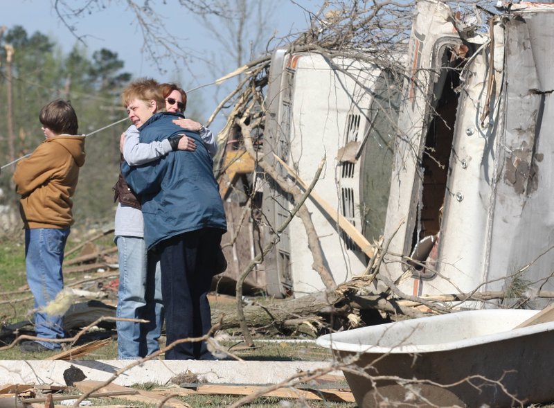 A woman, who said she was too grieved to talk (right) is comforted Saturday behind the ruins of a home in which Albert Shaw, 61, was killed when a  tornado that hit the downtown area of Mena Thursday evening.
