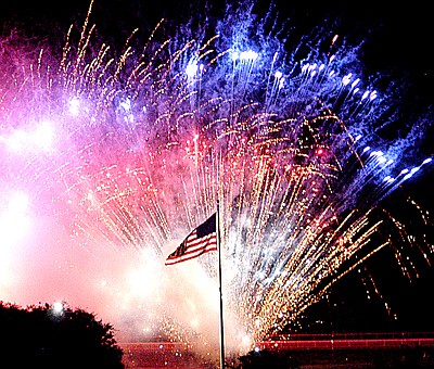 Red, white and blue fireworks explode as a backdrop to a U.S. flag during a patriotic display at Spa Blast in Hot Springs at Oaklawn Park. 