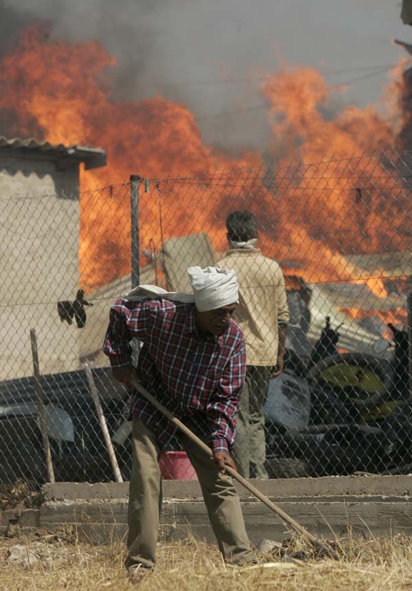 A man clears dry grass in front of his home as fire rages nearby in Dioni, 25 miles east of Athens, Greece, on Monday.