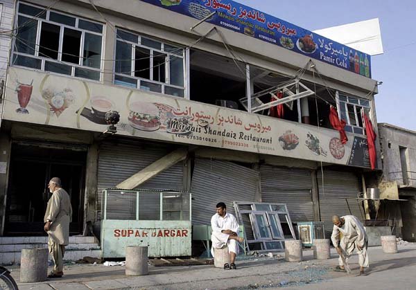Men stand below broken restaurant windows Wednesday after a blast in Kandahar, Afghanistan.