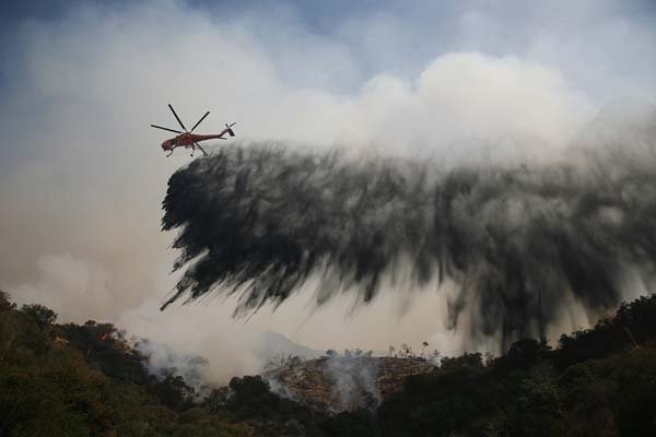 A helicopter drops water Friday as firefighters battle flames in Southern California's Angeles National Forest. Hundreds of California residents have fled wildfires, which covered 14,000 acres Friday. 