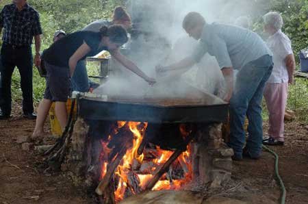 Magda Musur, left, and Billy Bower skim non-edible material off the top of cooking liquid sorghum as they help make sorghum molasses Saturday at the Cane Hill Harvest Festival. The festival continues today in Canehill.