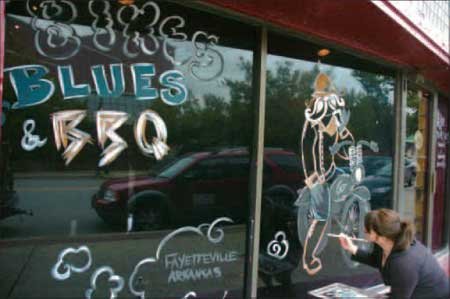 Joy Sagan, a server and artist with The Common Grounds, puts the final touches on a mural outside the longtime restaurant and bar in preparation for Bikes, Blues & BBQ.