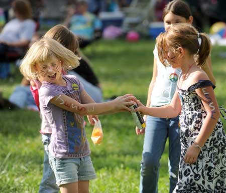 Jaden Jackson, 7, left, laughs as friend, Natalie Ricarte, 8, both of Mountainburg, sprays her with aerosol string while playing Sunday during the 27th annual Winfest at the Winslow ball fields.