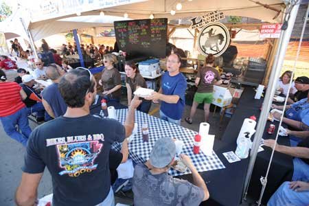 Don Bennett, a friend of the owner of Lucky Luke's BBQ, center, hands a sample rib to H.P. Wright, of Stilwell, Okla., as workers serve visitors to the 10th annual Bikes, Blues & BBQ motorcycle rally Friday in Fayetteville.