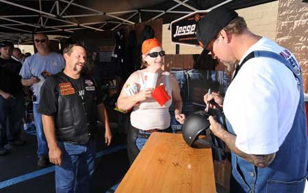 Jesse James, right, owner of West Coast Choppers and star of several motorcycle-related television shows, autographs a motorcycle helmet for Dena and Frank Smith of Joplin, Mo., during a stop to promote James' new line of clothing Sunday at the Wal-Mart Supercenter on West Martin Luther King Jr. Boulevard in Fayetteville. 