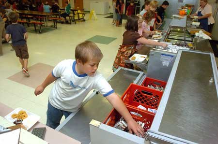 Third-grader Josh Dubois grabs a milk carton Monday during lunch at Root Elementary School in Fayetteville. A few area school districts have prohibited allowing students to eat now and pay later when their lunch balances dwindle because the schools could be treated like creditors under federal law. 