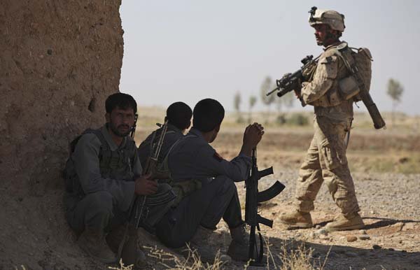 Afghan police sit in the shade as a U.S. Marine walks past during a joint patrol Tuesday in Nawa district, Helmand province in southern Afghanistan.