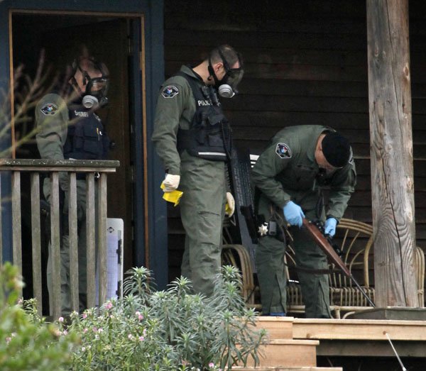 Sheriff's deputies look over a rifle they removed from a home where a suspect in the slaying of four police officers gunned down a day earlier was believed to have been, Monday.