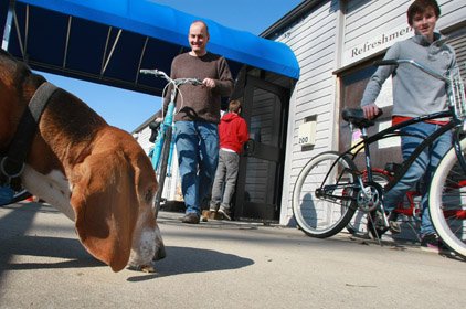 Amos, the Fike family’s basset hound, supervises as David Fike (left) and his son Allen, 15, roll bikes outside to entice customers while Fike’s younger son, Evan, 12, goes back inside River Trail Rentals for more.