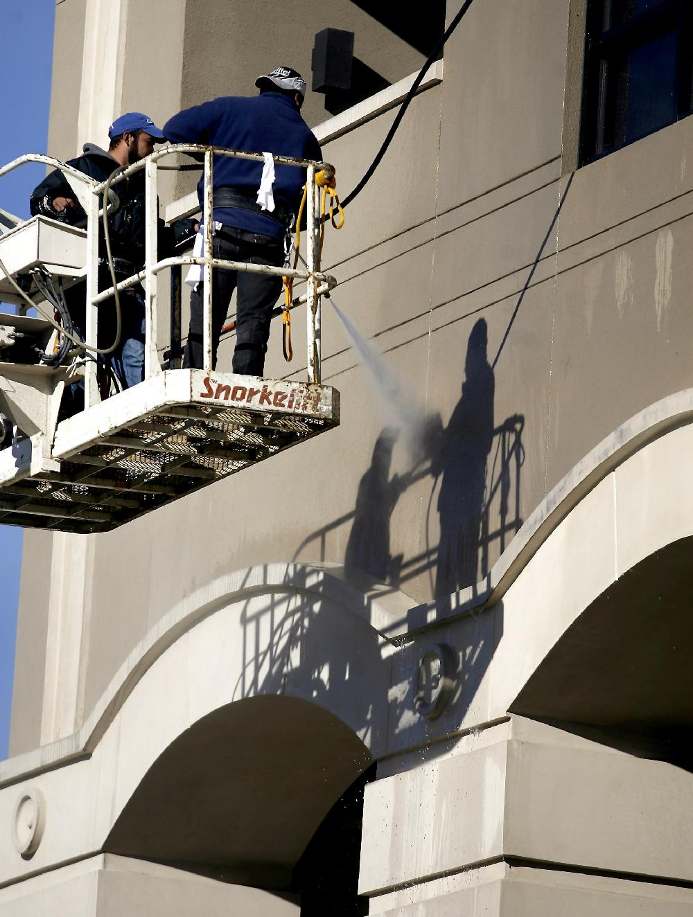 Arkansas Democrat-Gazette JASON IVESTER --122109--Yuvany Villarreal (cq) (left) and Humberto Movera (cq) pressure wash The Legacy Building Monday in Fayetteville. The pair are part of a group from R&H Painting working on the building's facade.