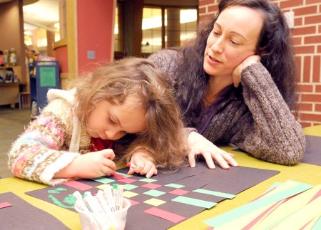 Alisha Chouinard watches Tuesday while her daughter, Dove Chouinard, 3, assembles and paints a Kwanzaa mat in the Children’s Library at the Bentonville Public Library.