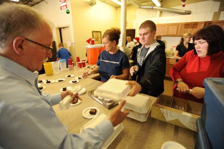 The Church at Arkansas members, from left, Jim Mitchell, Mary Frances Proctor, Kellen Summers and Debbie Beasley work to assemble and distribute meals Thursday at Seven Hills Homeless Center’s Day Shelter in Fayetteville.
