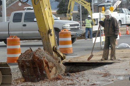 Florentino Rivera stands by to clear away dirt during sewer line work Tuesday at Eighth and Poplar streets in Rogers. Sewer lines in the intersection area, some 50 years old, are being replaced. The work at Eighth and Poplar is the first step in a long project to replace aging concrete sewer lines in Rogers.