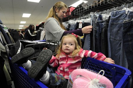 Adeline Patterson, 2, kicks back in a shopping cart Thursday as her mother, Aubrey, searches for clothes for their six-member family during the grand opening of the Goodwill Store and Donation Center in Bentonville.
