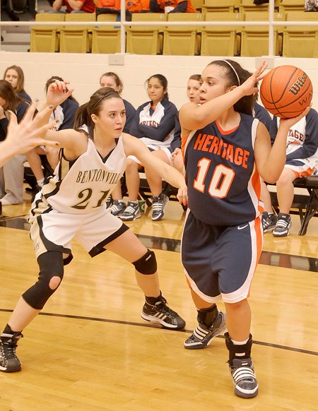 Rogers Heritage guard Yalile Johnson, right looks for passing room from the corner while guarded by Bentonville’s Emily Spencer during a game on Feb. 23 in Bentonville.
