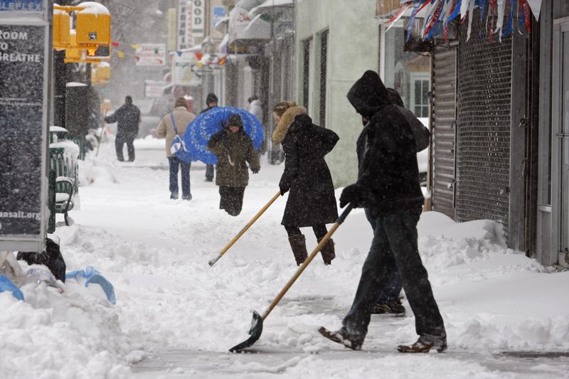 People shovel snow off a sidewalk in front of businesses as pedestrians make their way during a snowstorm in the Brooklyn Borough of New York, on Friday, Feb. 26, 2010. 