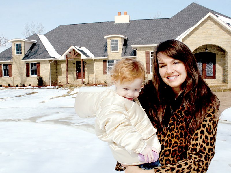 Katie Wilson, with her 2-year-old daughter, Neva Kate, stands in front of their house in Mountain Home that has been awarded the first Green Building Standard certification in Arkansas from the National Association of Home Builders.