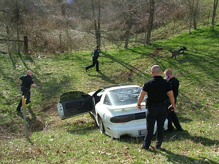 Benton County Sheriff’s deputies D. Winn and Corey Coggin, deputies first class, watch the car and suspect while Pea Ridge police officers Chris Olson and Mike Marler follow Jazz, a Pea Ridge police dog, who picked up the scent of the two men who fled from the wrecked Pontiac which had led law enforcement officers from several agencies from both Arkansas and Missouri on a high-speed pursuit.