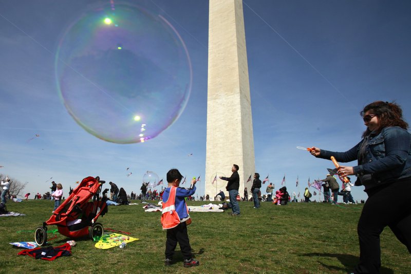 Claudia Sandoval Wright, right, of Alexandria, Va., blows soap bubbles for children to catch by the Washington Monument on the opening day of the National Cherry Blossom Festival in Washington, on Saturday.