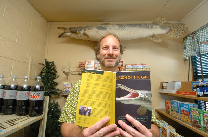 Mark Spitzer, a University of Central Arkansas teacher and author of Season of the Gar, shows a copy of his book inside S&K Bait and Grocery at Lake Conway, where a mounted alligator gar hangs on the wall.