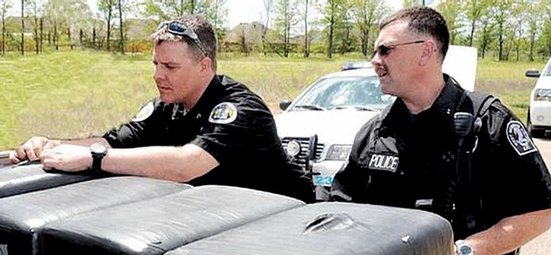 In this April 8 photo from the West Memphis Times, West Memphis police officers Brandon Paudert (left) and Bill Evans, both members of a special unit combating drug trafficking on highways, examine bags during a traffic stop. Both men were killed during a traffic stop Thursday.