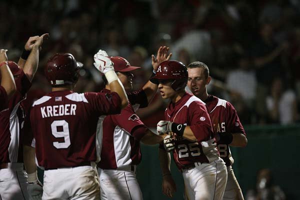 Arkansas outfielder Collin Kuhn is greeted at home plate after a ninth-inning home run that made the score 6-4, the eventual winning margin over Washington State. The victory left the Razorbacks waiting for the winner in an elimination game between Washington State and Kansas State.