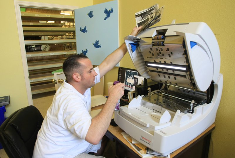 Chris Clevidence (above) cleans a scanner while digitizing photos from newspaper archives at John Rogers Archive in North Little Rock. Rogers (below left) has collected millions of photos. Photos are cleaned by (below right) Ross Quinn, Evan Blake and Brittani Bennett to get them ready for scanning as Rogers (in background) checks the prints.