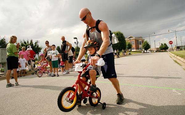 Noah Freisen, 3, crosses the three-mile finish line with a little help from his father, Shawn Friesen. The Freisens, who live in Bentonville, joined more than 400 other cyclists, walkers and joggers for Satruday morning's Tour de Fun, an annual event that raises money for the Teen Action Support Center.